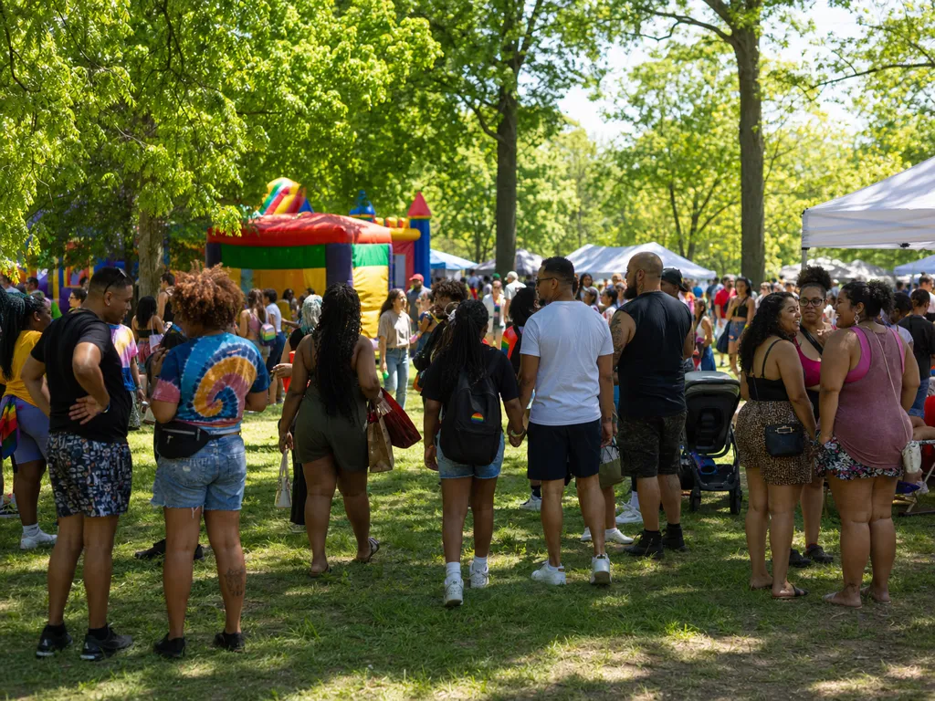 Families gather on a sunny park lawn near colorful inflatable bounce houses and vendor tents at a community summer festival.