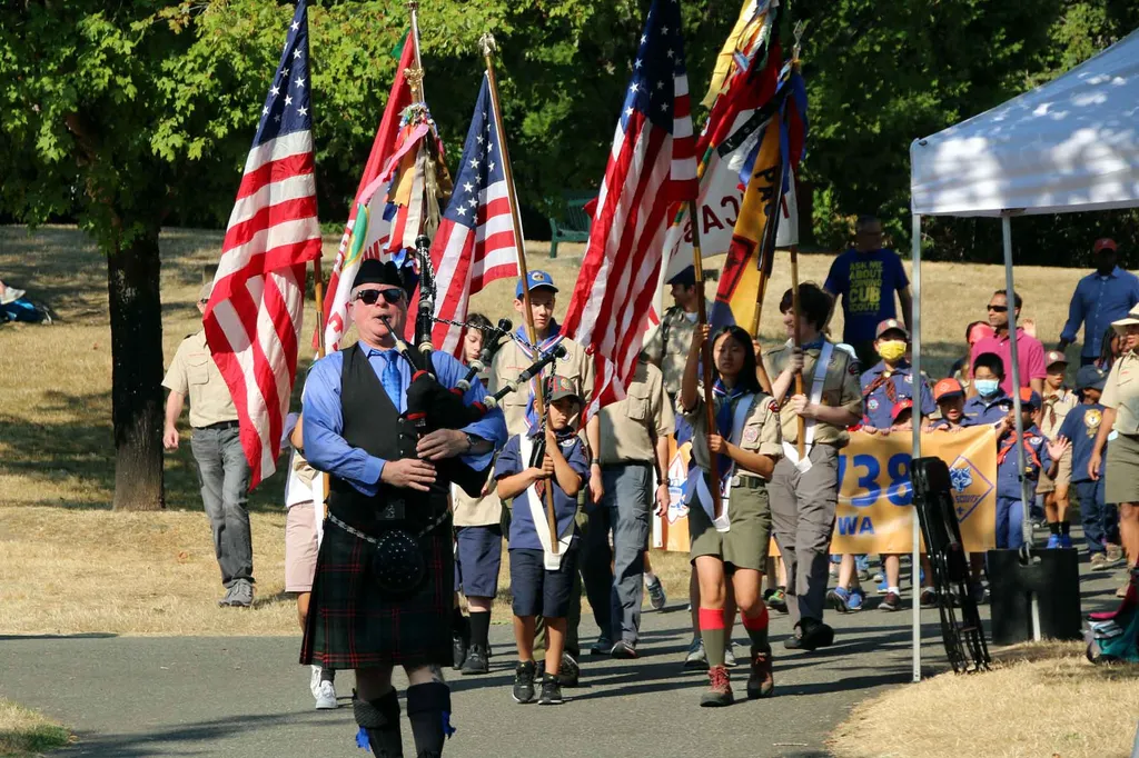 A bagpiper leads a community parade during an outdoor festival celebration at a local park.