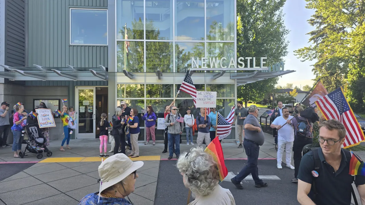 A group of people gathered outside Newcastle City Hall, with some holding Pride flags and others holding American flags and signs reading "We stand united under the USA flag."