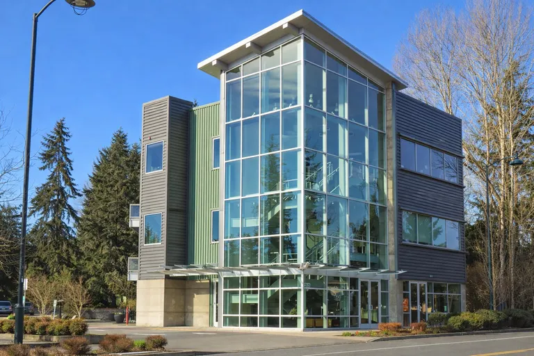 Newcastle City Hall exterior on a cloudy Pacific Northwest afternoon, a municipal building with a parking lot and evergreen trees in the foreground.