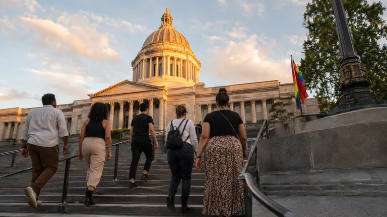 The Washington State Capitol dome in Olympia rises against a warm evening sky, with a small pride flag visible near the entrance steps.